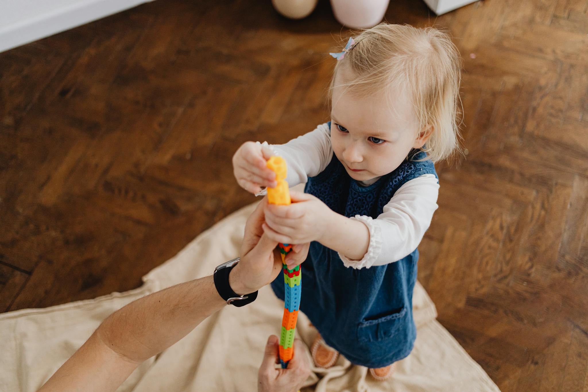 A young girl intently plays with colorful building blocks indoors, focusing and learning.