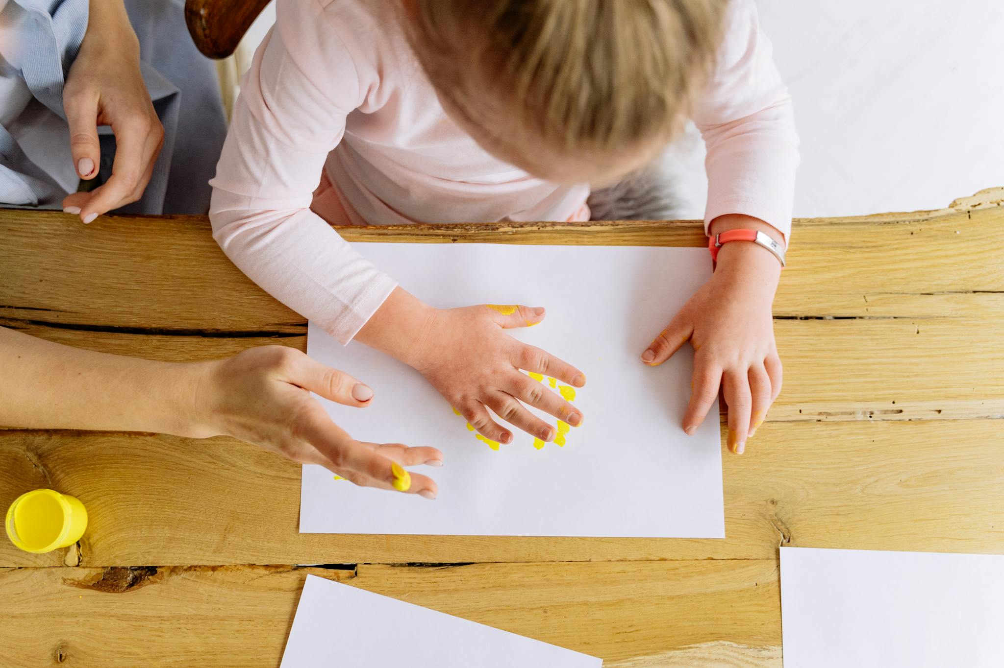 Overhead view of a child finger painting on paper indoors, fostering creativity and fun.